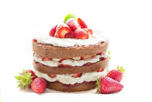 A three-layered cake sandwiched with cream and strawberries, with a small mound of strawberries on top and to the sides